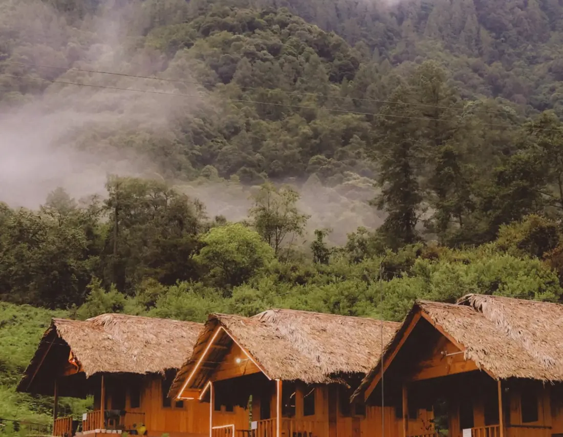 Thatched wooden cottages below misty hills in Anini