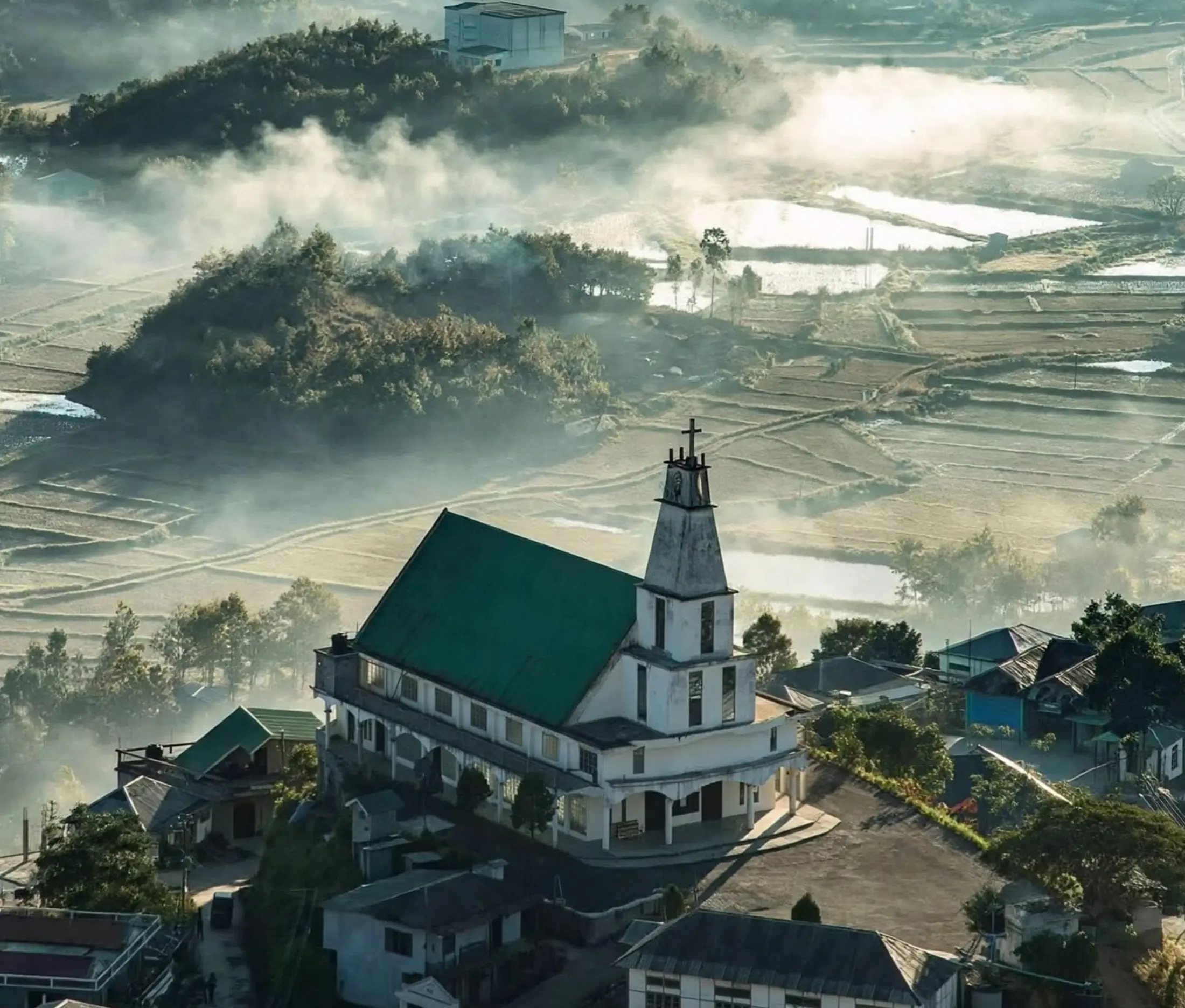 Mist lifting off terraced valleys around a hilltop church in Mizoram