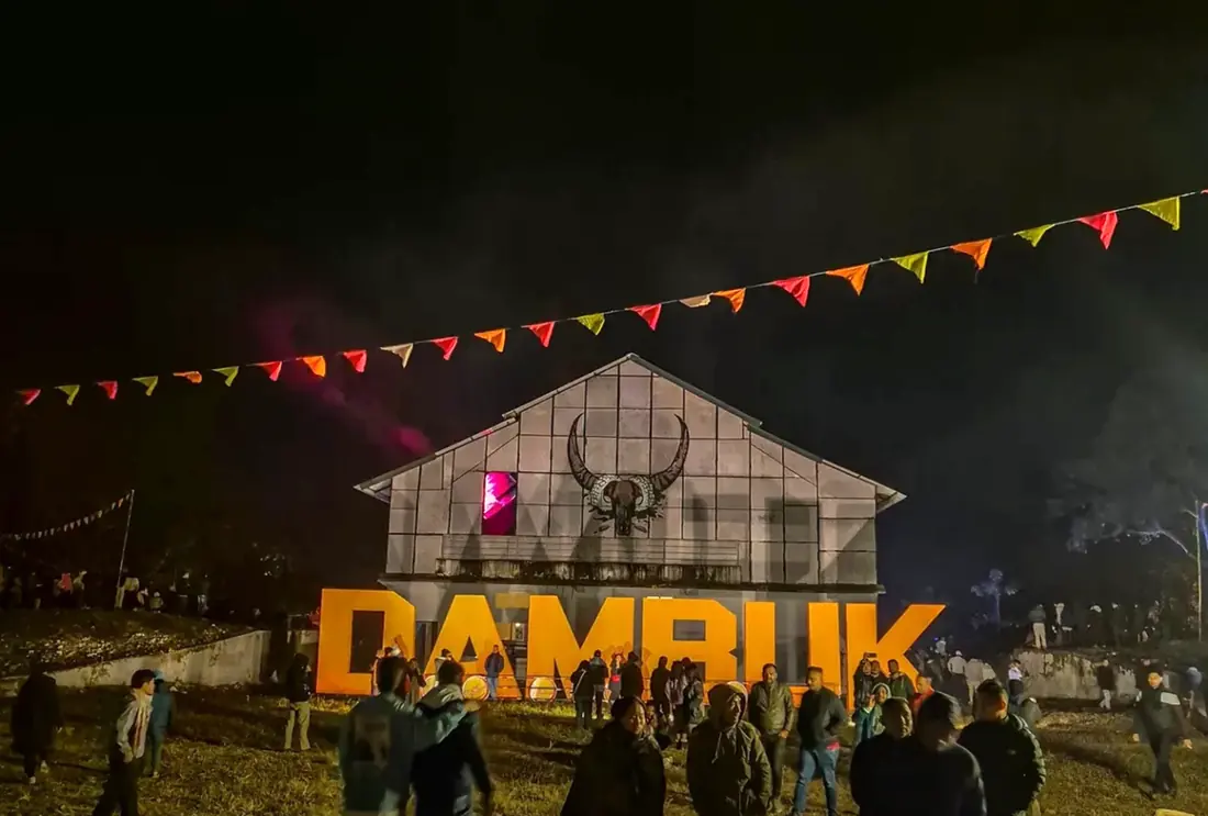 The Dambuk sign lit up at night under festival flags